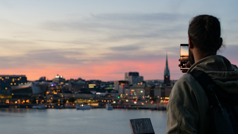 Man som fotar en kvällsbild över Stockholm genom sin mobil