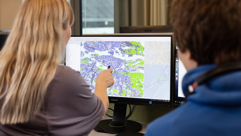 Två personer sitter med ryggen åt kameran och tittar in i en skärm med Stockholmskarta