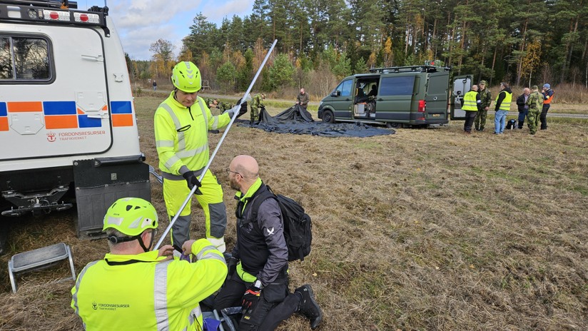En grupp män i arbetsskyddskläder och hjälmar arbetar på ett fält