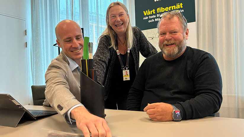 Två män och en kvinna vid ett konferensbord med en modell som visar fiberkablar i ett plaströr.
